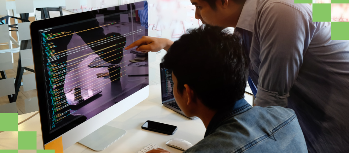 two-male-coworkers-leaning-over-desk-looking-at-lines-of-code-on-a-computer-monitor-discussing-task-automation